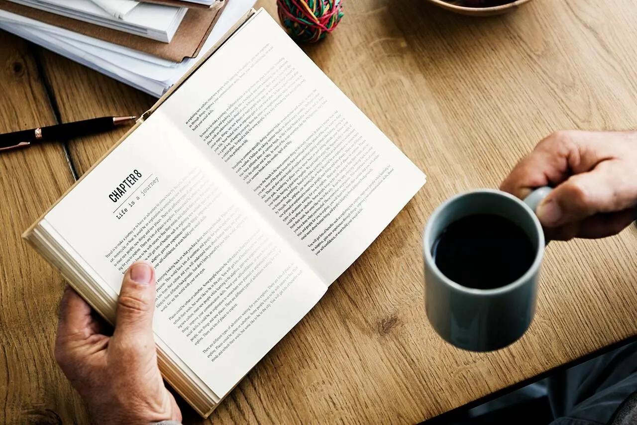 Libro abierto y taza de café sobre una mesa de madera