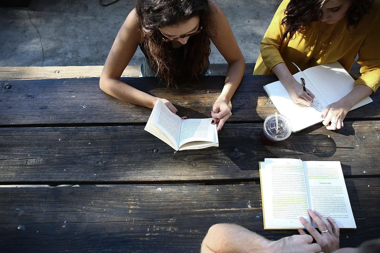 Dos estudiantes leyendo y tomando apuntes en una mesa de madera